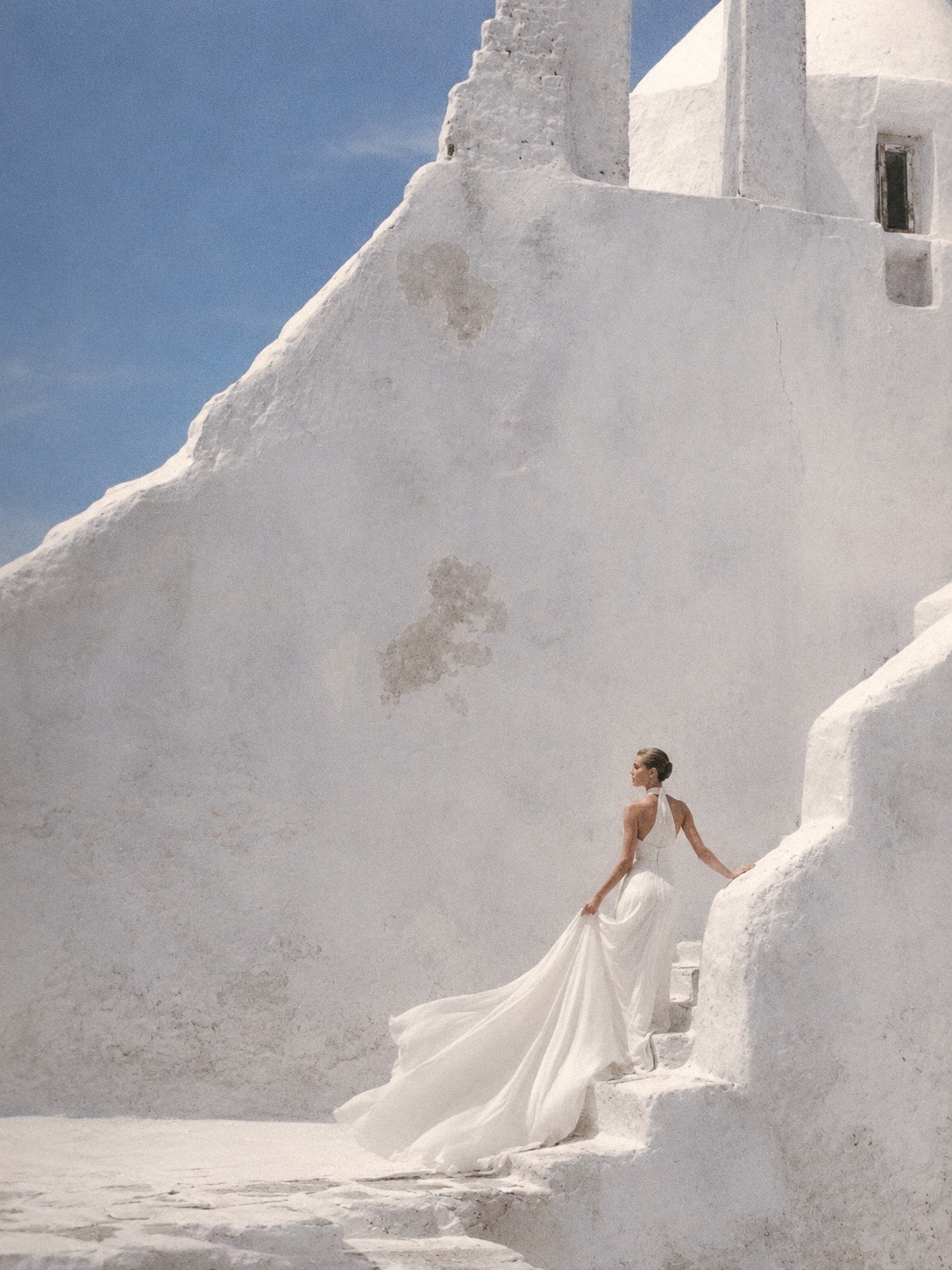 Bride on whitewashed steps under a clear blue sky